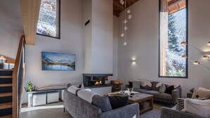 A modern living room with a fireplace, large windows, and a staircase. - Modern chalet in Morzine, 12 pers, 5 br, near center (Morzine)