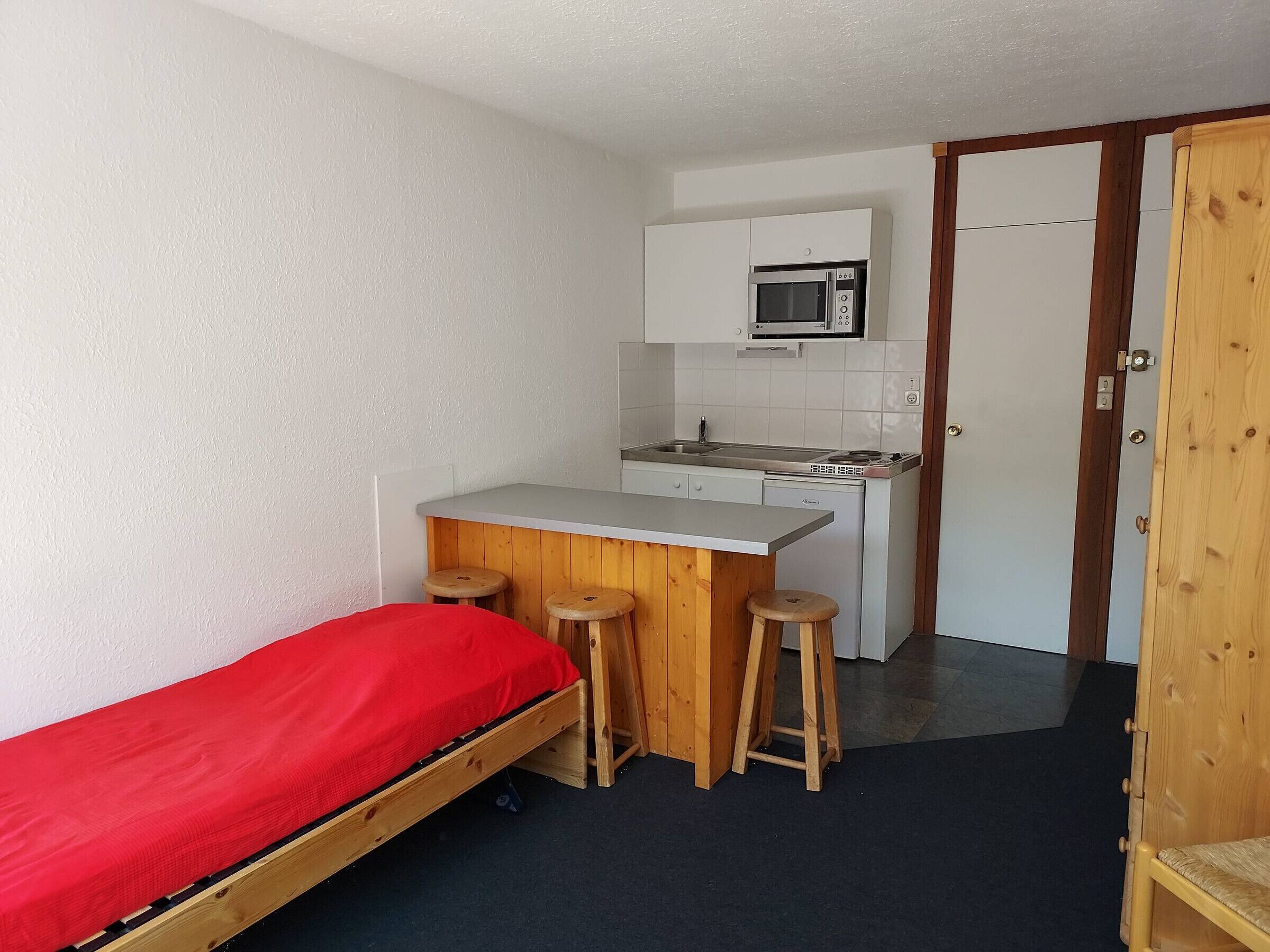 Una habitación compacta con cama, una kitchenette pequeña y una barra de taburete de madera.