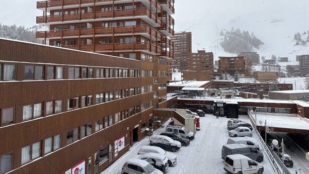Ein mehrgeschossiges Gebäude mit modernem Design, ausgestattet mit Balkonen und einem Parkplatz mit mehreren Autos.