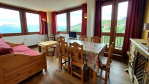 A cozy room with a bed, a dining table, and chairs. There is a TV and a window with a view of the mountains. - Comfortable apartment, close to slopes, pets allowed (La Plagne-Tarentaise)