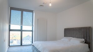 A bedroom with a large window, a bed, and a radiator. - Luxury two Bedroom Apartment (Barking)