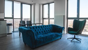 A modern living room with a blue sofa, a green chair, and a dining table. - Luxury two Bedroom Apartment (Barking)
