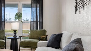 En stue med sofa, to lænestole, et lille rundt bord og en hængende plante.