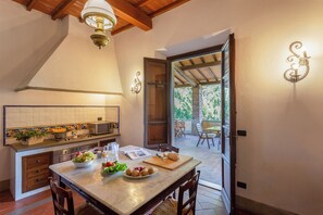 A kitchen with a marble countertop, a dining area with a table and chairs, and a view of the outdoors through an open door. - Villa Maltempo (Vicchio)