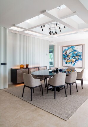 Un espace de salle à manger moderne avec une table ronde, six chaises et un lustre contemporain.