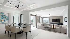 A modern living room with a large sofa, a dining table with chairs, and a TV mounted on the wall. - Villa la Vista Marbella (Marbella)