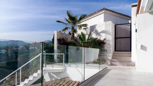 A modern balcony with glass railings, a white exterior wall, and a view of the surrounding landscape. - Villa la Vista Marbella (Marbella)