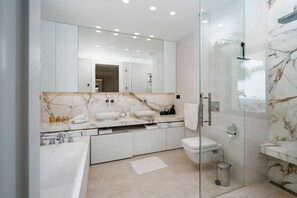 Une salle de bain moderne avec un grand miroir, deux lavabos, une baignoire et une douche à l’italienne.