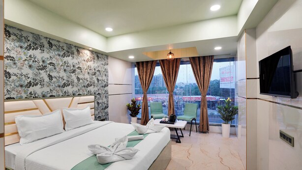 A hotel room with a bed, a TV, a table with chairs, a window with curtains, and a view of the city.