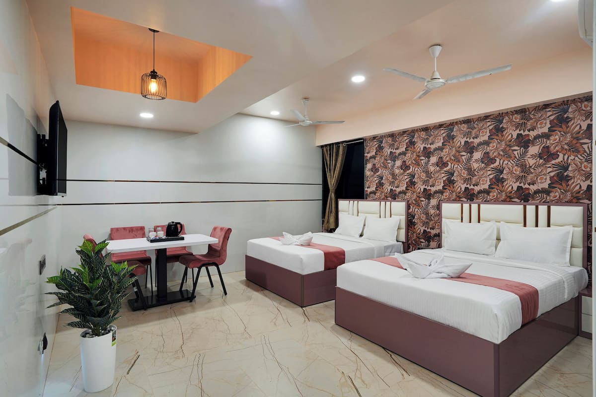 A hotel room with two beds, a dining table, chairs, a potted plant, and a ceiling fan.