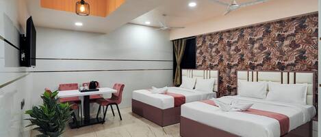 Une chambre d’hôtel avec deux lits, une table à manger, des chaises, une plante en pot et un ventilateur de plafond.