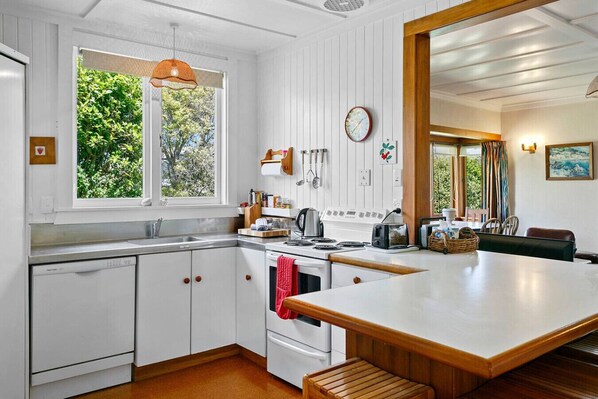 Une cuisine moderne avec des meubles blancs, un grand îlot central et une vue sur la verdure à l’extérieur.