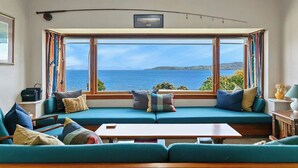 A cozy living room with a large window overlooking a scenic view of the sea and hills.