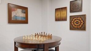 Una habitación con una mesa redonda de madera que muestra un juego de ajedrez, un cuadro enmarcado y tres obras de arte adicionales en la pared.