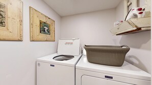 Un área de lavandería con una lavadora y secadora Maytag, una cesta de mimbre sobre la secadora y dos cuadros en la pared.