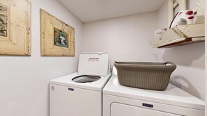 A laundry area with a Maytag washer and dryer, a wicker basket on the dryer, and two framed pictures on the wall.