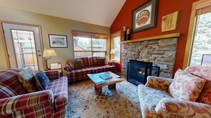 A cozy living room with plaid sofas, a fireplace, and a stone wall.
