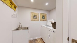A compact kitchen with a sink, a washing machine, and two framed pictures on the wall.