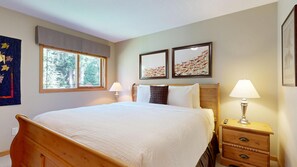 A bedroom with a wooden bed, bedside tables, a window with a view of trees, and two framed artworks on the wall.