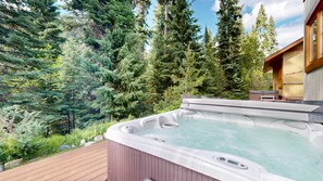 A hot tub on a wooden deck surrounded by a forest.