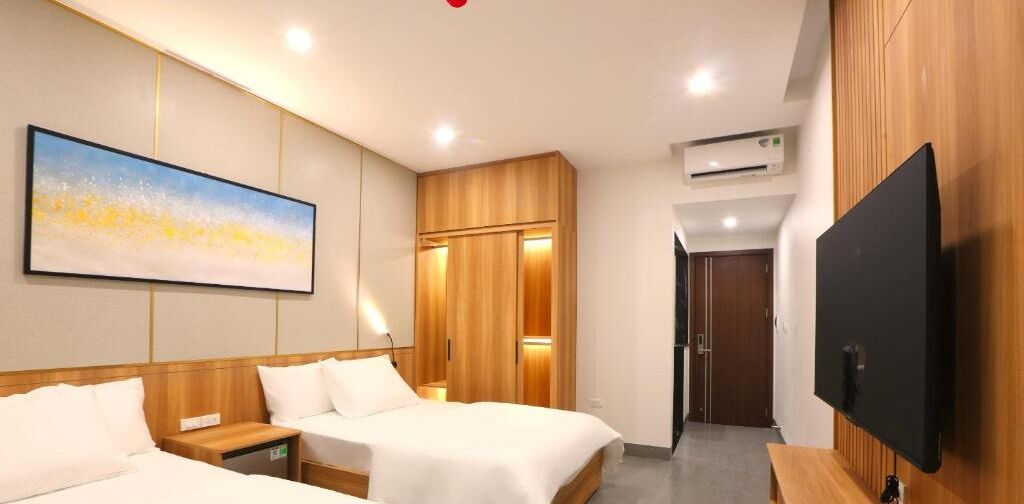 A hotel room with two beds, a flat-screen TV, wooden paneling, and a painting on the wall.