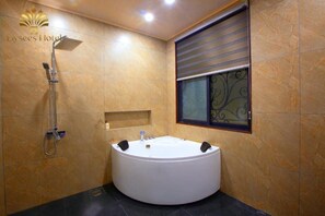 A modern bathroom with a large bathtub, a showerhead, and a window with decorative ironwork. - Elysees Hotel (Sam Son)