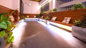 A well-lit indoor space with a long bench along the wall, surrounded by potted plants and a wooden bench area. - Elysees Hotel (Sam Son)