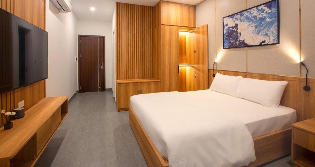 A hotel room with a large bed, wooden wardrobe, a television on the left, and a painting on the wall.