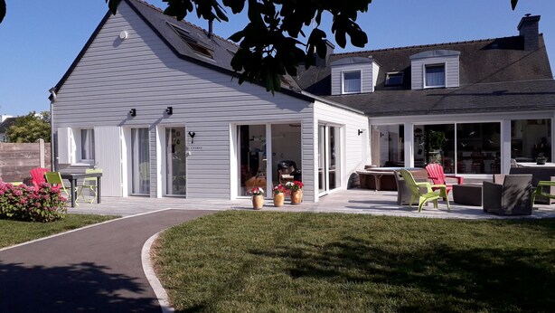 A two-story house with a covered patio, a lawn, and outdoor furniture. - Gîte PMR Balade Océane Lodonnec (Loctudy)