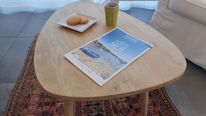 A wooden table with a magazine, a plate with cookies, and a cup. - Gîte PMR Balade Océane Lodonnec (Loctudy)