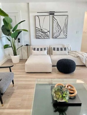 A modern living room with a sofa, a coffee table with a plant, and abstract wall art.
