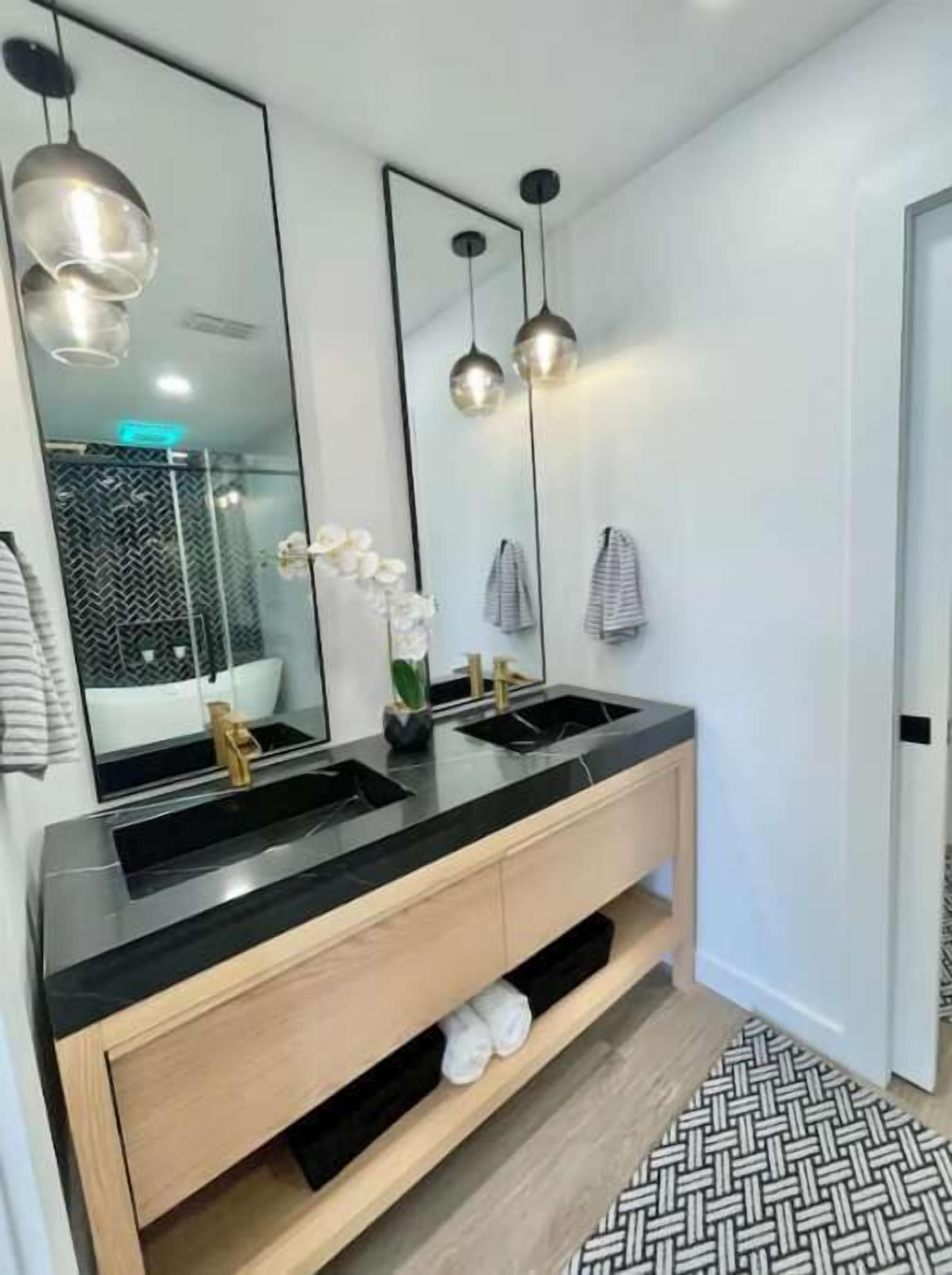 A modern bathroom with a black vanity, two sinks, a large mirror, and pendant lighting.