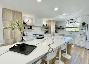 A modern kitchen with white cabinetry, a marble countertop, and a central island with bar stools.