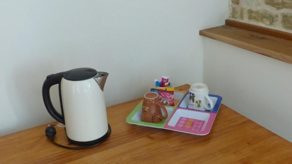 Une petite table sur laquelle se trouvent une bouilloire électrique blanche, une tasse marron, une boîte de mouchoirs, une tasse de café et une calculatrice jouet.