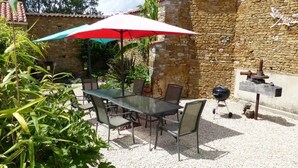 Een terras buiten met een tafel, stoelen en een rood-witte parasol, plus een stenen muur.