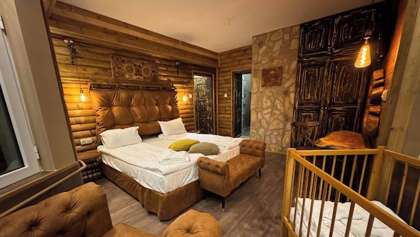 A log cabin-style bedroom with a large bed, two armchairs, a wooden crib, and a stone accent wall. - The Luxurious Forest Villa Borovets - 8 Bedroom Chalet (Samokov)