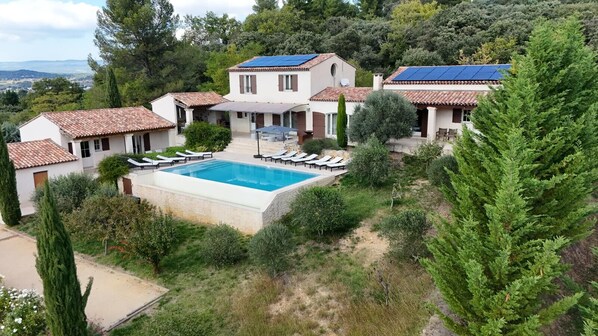 Une villa dotée d’une piscine, entourée de chaises longues, d’un jardin et offrant une vue sur la campagne.