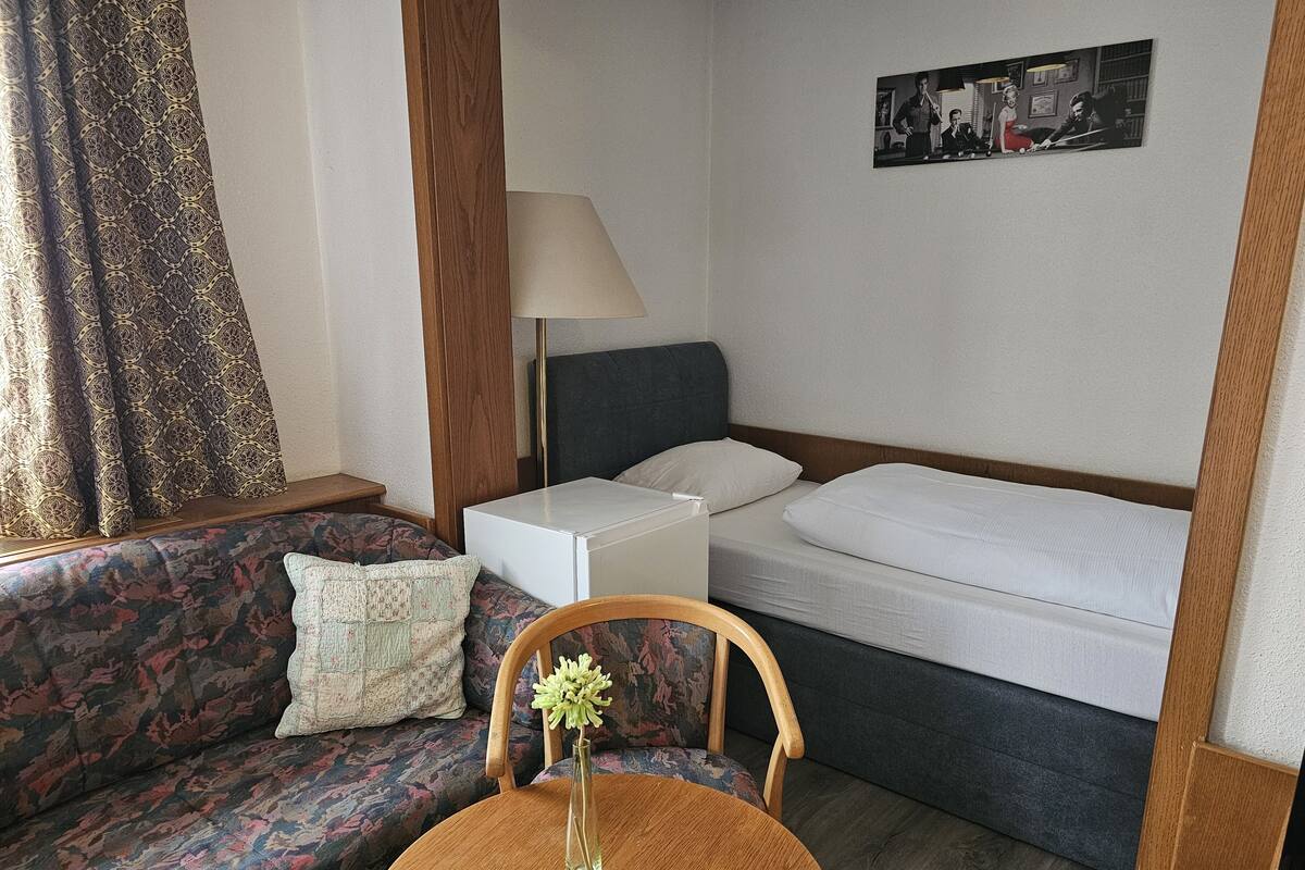 Habitación de hotel con sofá, una mesita con un florero, mesita de noche, lámpara y cama.