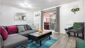 A modern living room with a grey sectional sofa, a glass coffee table, and a green armchair.