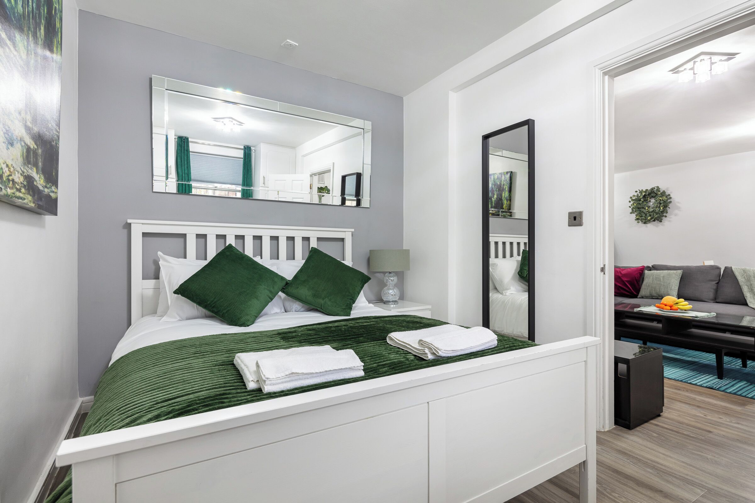 Une chambre à coucher moderne avec un lit blanc, des oreillers verts, une couvre-lit verte et une table de chevet blanche avec une lampe.