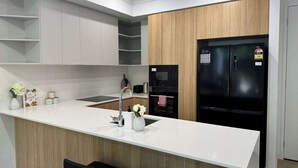 A modern kitchen with a white countertop, wooden cabinets, a black refrigerator, and a built-in oven. - Stylish Family 3BR  in Central Hope Island, Family (Hope Island)