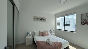 A bedroom with a bed, a nightstand, a window, and a door. - Stylish Family 3BR  in Central Hope Island, Family (Hope Island)