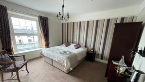 Ein Schlafzimmer mit Bett, Stuhl, Nachttisch, Kommode, Fenster und einer gestreiften Wand.