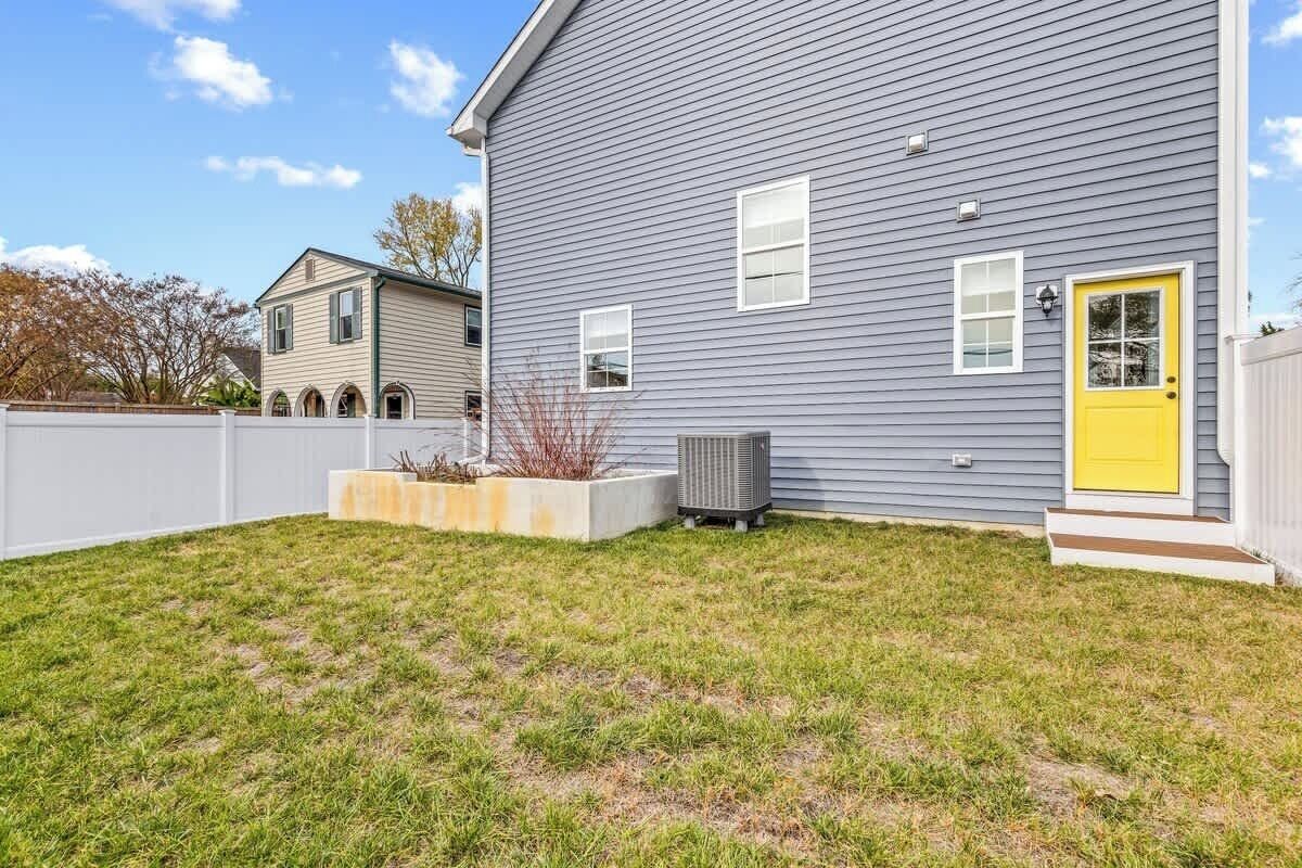 A residential house with a grey siding exterior, a yellow front door, and a small front yard with grass and a planter.