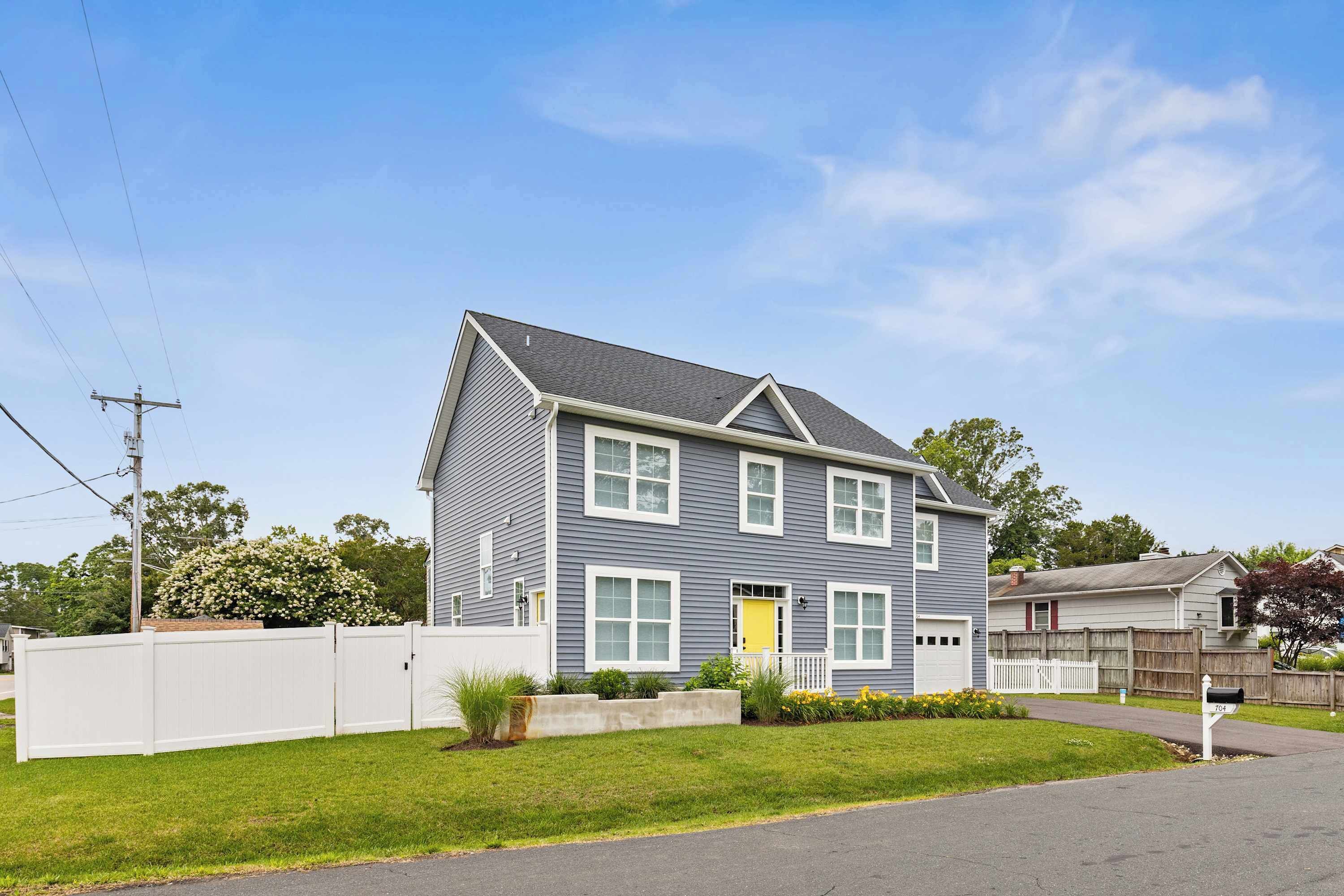 A two-story residential house with a grey siding exterior, white trim, and a yellow front door.