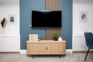 Una sala de estar moderna con un televisor de pantalla plana montado en la pared, un mueble de madera con una planta y una pared azul de acento.