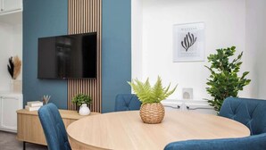 Une salle de réunion moderne équipée d’une table ronde, de chaises bleues, d’un téléviseur et de plantes décoratives.