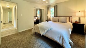 Quarto com cama, mesas de cabeceira, ventilador de teto e janela com cortinas.