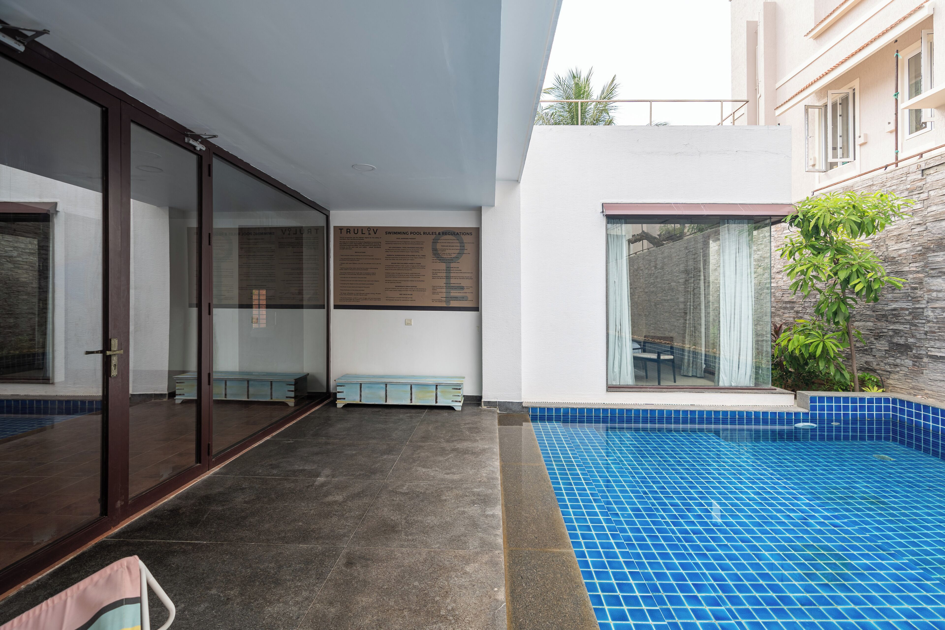A modern hotel interior with a swimming pool, a glass door entrance, and a stone wall.