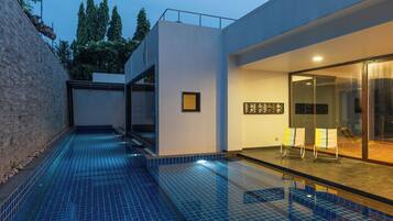 Relax by the pool surrounded by a minimalist building and lush garden.